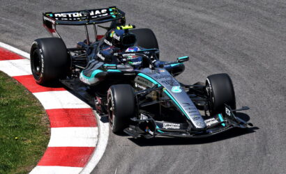 Mercedes F1 car from the Petronas team rounding a left-hand corner on a racetrack, red-and-white curbs in view