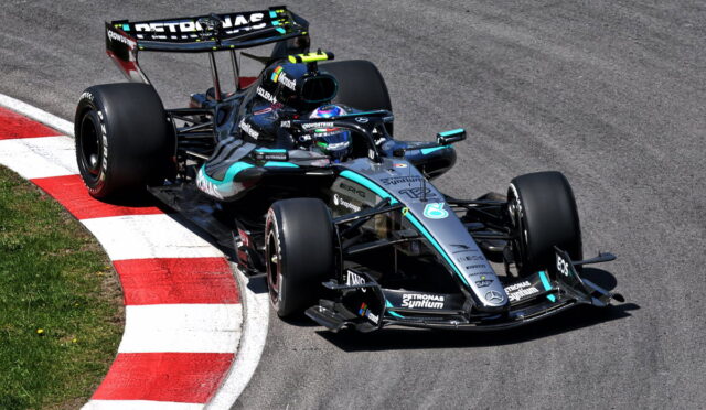 Mercedes F1 car from the Petronas team rounding a left-hand corner on a racetrack, red-and-white curbs in view