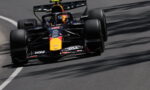 Red Bull Racing Formula 1 car speeding along a race track, yellow nose and sponsor logos visible on a dark blue chassis.