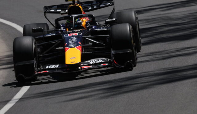 Red Bull Racing Formula 1 car speeding along a race track, yellow nose and sponsor logos visible on a dark blue chassis.