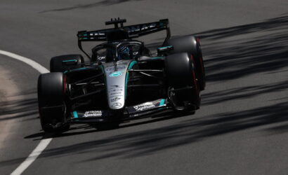 Mercedes F1 race car (black-teal livery) navigating a curve on track, sponsor logos visible on the nose and sidepods