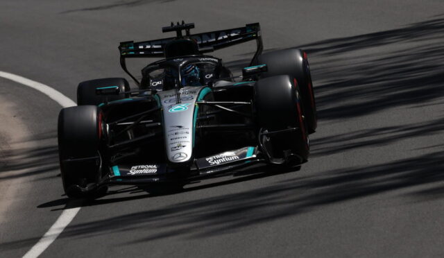 Mercedes F1 race car (black-teal livery) navigating a curve on track, sponsor logos visible on the nose and sidepods