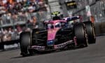 Pink Formula 1 car speeding on a race track with spectators blurred in the background, ready for a pit stop or overtaking maneuver.