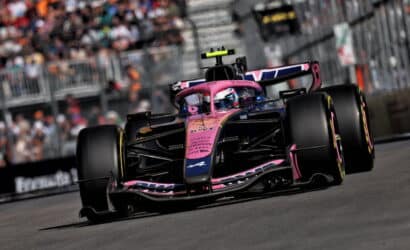 Pink Formula 1 car speeding on a race track with spectators blurred in the background, ready for a pit stop or overtaking maneuver.
