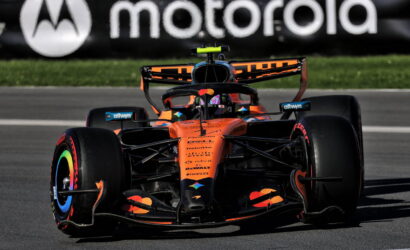 Orange McLaren Formula 1 car racing on a track with a Motorola banner in the background.