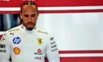 Male Formula 1 driver in a white Ferrari suit with sponsor logos (HP, Shell, UniCredit) standing against a red-white backdrop, looking down.