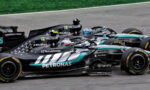 Three black Mercedes Formula 1 race cars with Petronas livery speeding on a track, sponsors visible on the chassis and helmets.