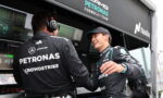 Two Mercedes-AMG Petronas Formula 1 team members shake hands in the pit with telemetry screens and branding in the background.