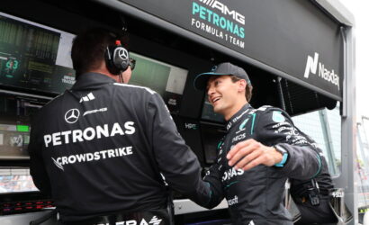 Two Mercedes-AMG Petronas Formula 1 team members shake hands in the pit with telemetry screens and branding in the background.