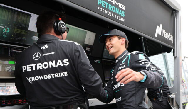 Two Mercedes-AMG Petronas Formula 1 team members shake hands in the pit with telemetry screens and branding in the background.