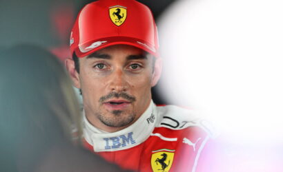 Male racing driver in a red Ferrari cap and suit being interviewed by the media.