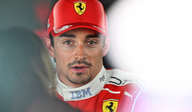 Male racing driver in a red Ferrari cap and suit being interviewed by the media.