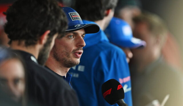 Driver wearing blue cap speaks to press, microphone with red F1 logo in foreground.