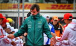 Formula E team member in a teal jacket greets and shakes hands with fans in white uniforms along the pit wall, DHL signage in the background