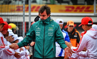 Formula E team member in a teal jacket greets and shakes hands with fans in white uniforms along the pit wall, DHL signage in the background