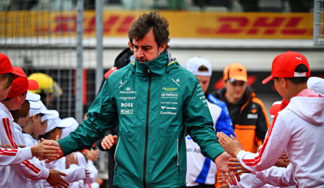 Formula E team member in a teal jacket greets and shakes hands with fans in white uniforms along the pit wall, DHL signage in the background