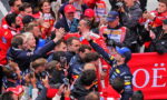 Group of Formula 1 drivers in racing suits exchanging high-fives amid cheering fans and photographers.