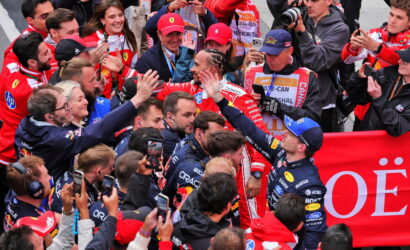Group of Formula 1 drivers in racing suits exchanging high-fives amid cheering fans and photographers.