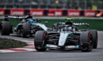 Two Mercedes Formula 1 cars navigate a tight corner on the race track, foreground car leading with Petronas logos in view.