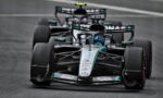 Mercedes Formula 1 car in Petronas livery racing on a track, with another car close behind in the background, front view.