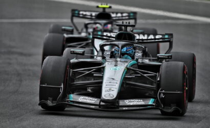 Mercedes Formula 1 car in Petronas livery racing on a track, with another car close behind in the background, front view.