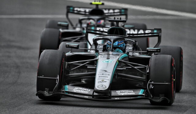 Mercedes Formula 1 car in Petronas livery racing on a track, with another car close behind in the background, front view.
