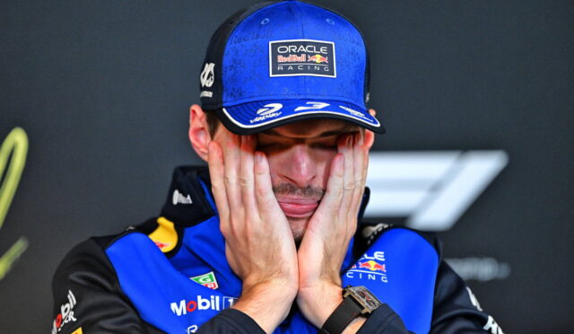 Race car driver in a blue Oracle Red Bull Racing cap and suit, hands pressed to his cheeks in a stressed expression.