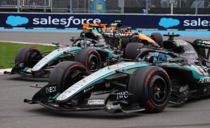Three Mercedes Formula 1 cars race side by side on a track, with a blue Salesforce banner in the background.