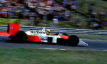 Red and white Marlboro-liveried Formula 1 car, number 12, speeding on a race track with a blurred grandstand backdrop.