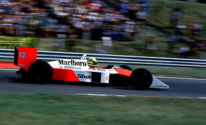 Red and white Marlboro-liveried Formula 1 car, number 12, speeding on a race track with a blurred grandstand backdrop.