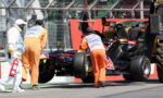 Pit crew in orange overalls push a Red Bull Formula 1 car while a safety worker in white carries a fire extinguisher nearby after an incident.