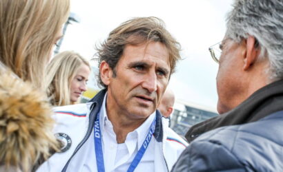 Man in a white BMW jacket speaks with a gray-haired man wearing glasses at an outdoor event, blue lanyard around his neck