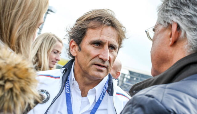 Man in a white BMW jacket speaks with a gray-haired man wearing glasses at an outdoor event, blue lanyard around his neck