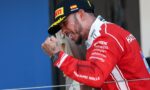 Male cyclist in a red racing suit and black cap rests his head on a wooden panel during a podium moment.