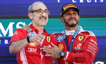 Two Ferrari Formula 1 drivers pose on the podium with medals after a race, smiling at the camera.
