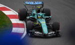 Green Formula 1 race car navigates a corner on a racetrack, red-and-white curb visible on the inside. Sponsor logos shown on the body and wing.