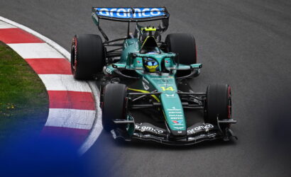 Green Formula 1 race car navigates a corner on a racetrack, red-and-white curb visible on the inside. Sponsor logos shown on the body and wing.