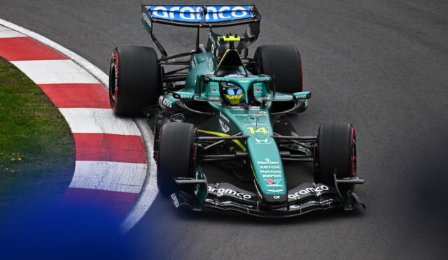 Green Formula 1 race car navigates a corner on a racetrack, red-and-white curb visible on the inside. Sponsor logos shown on the body and wing.