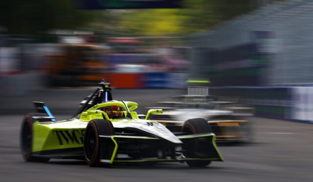 Neon-yellow Formula 1 car speeds along a race track, with a second car blurred in the background during a tight corner.