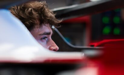 Close-up of a man with brown hair, looking to the left inside a red vehicle cockpit corner.