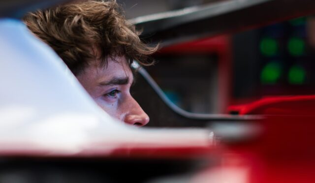 Close-up of a man with brown hair, looking to the left inside a red vehicle cockpit corner.