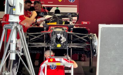 Ferrari Formula 1 race car in a garage with crew members studying blueprints or notes nearby.