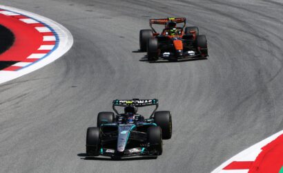 Three Formula 1 cars race through a sharp corner on a track, with red-and-white curbs along the inside edge.