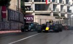 Two Formula 1 cars race side by side on a city street circuit with sponsor barriers and a building backdrop, Qatar Airways banners visible.