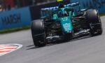 teal Formula 1 car on a race track, turning into a corner with sponsor decals visible