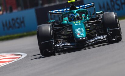 teal Formula 1 car on a race track, turning into a corner with sponsor decals visible