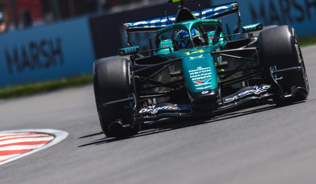 teal Formula 1 car on a race track, turning into a corner with sponsor decals visible