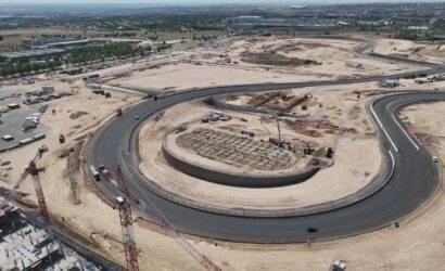 Aerial view of a large construction site with a circular road and a central ring, cranes, and heavy equipment at ground level.
