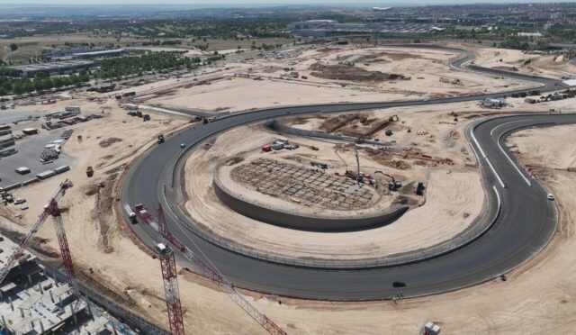 Aerial view of a large construction site with a circular road and a central ring, cranes, and heavy equipment at ground level.