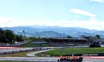 Race car with Oracle Red Bull livery speeding around a track with mountains in the background, under a blue sky.